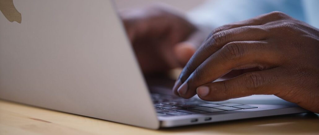 Hände tippen eine Suchanfrage auf einer Laptop-Tastatur